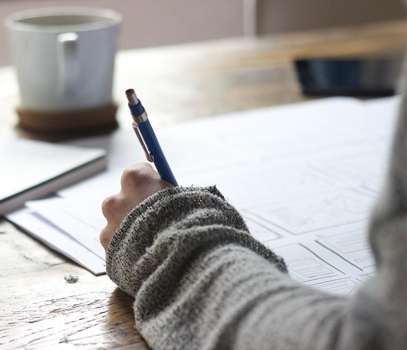 person's hand writing on table with coffee cup